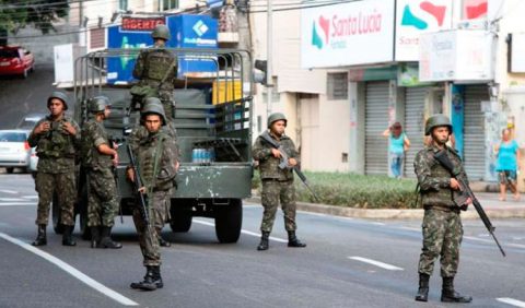 Um caminhão do exército e sete soldados armados andam por uma rua.