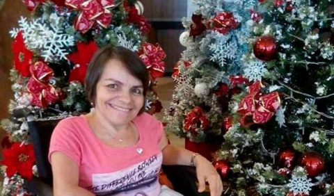 Mulher em cadeira de rodas, sorrindo, ao lado de uma árvore de Natal