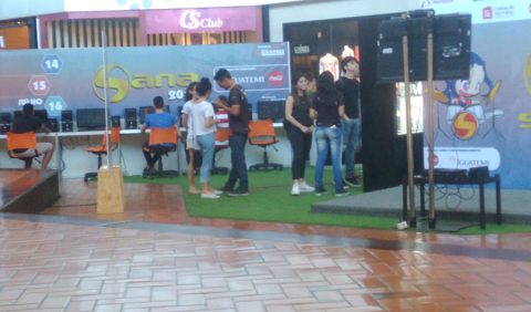 Visão frontal da praça de exposições do Shopping Iguatemi, com o nome Sana 2017 à esquerda em um grande banner, pessoas conversando e jogando vídeo game