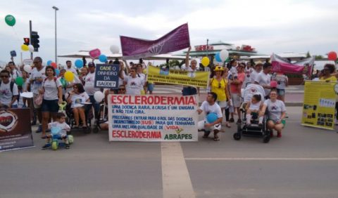 Grupo de pessoas - homens, mulheres e crianças - carregando faixas e usando camisetas alusivas ao Dia Mundial das Doenças Raras