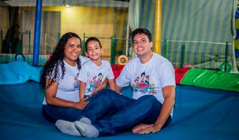 Foto horizontal em um brinquedo de pula pula, com três pessoas: um casal e um garotinho sentado no colo da mãe, entre os dois.