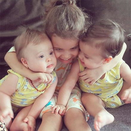 Três irmãs brincam e se abraçam afetuosamente. À esquerda, Luíza tem Síndrome de Down, é gêmea de Lívia, à direita. Ao centro, Laura, a mais velha